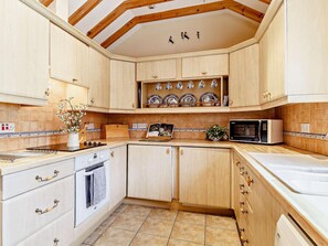 A kitchen with wooden cabinets, a stove, a microwave, and a tiled backsplash. - 2 Bed in Dereham (oc-57133) (Mattishall)