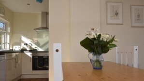 Et køkken med et træbord, en vase med blomster og billeder på væggen.
