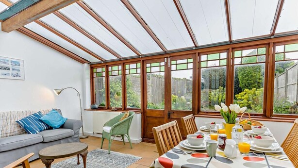 Ein Wintergarten mit Esstisch, gedecktem für ein Frühstück, einer Couch und einem Sessel.