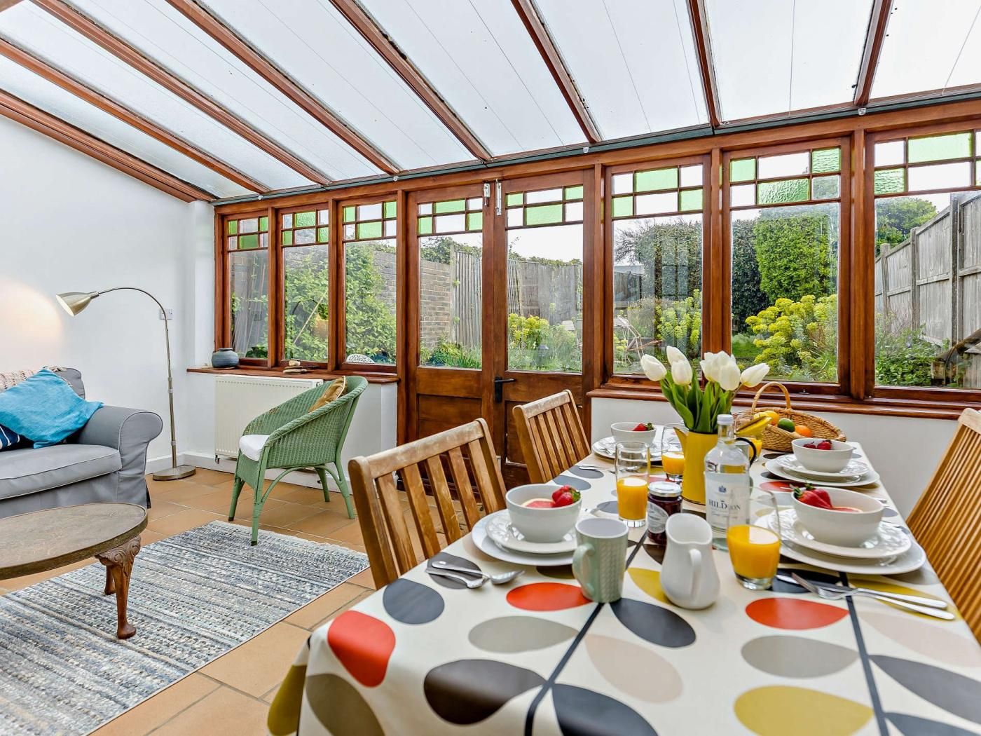 A dining area with a table set for breakfast, large windows, and a view of the garden.