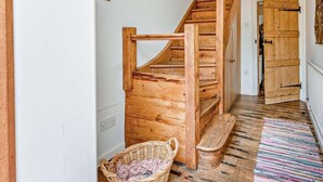 Eine Holztreppe führt zu einem Raum mit einer weißen Wand, einem Korb und einem farbenfrohen Streifen Teppich.