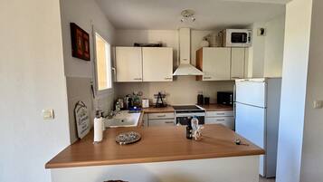 A kitchen with white cabinets, a wooden countertop, a microwave, a refrigerator, and a window.