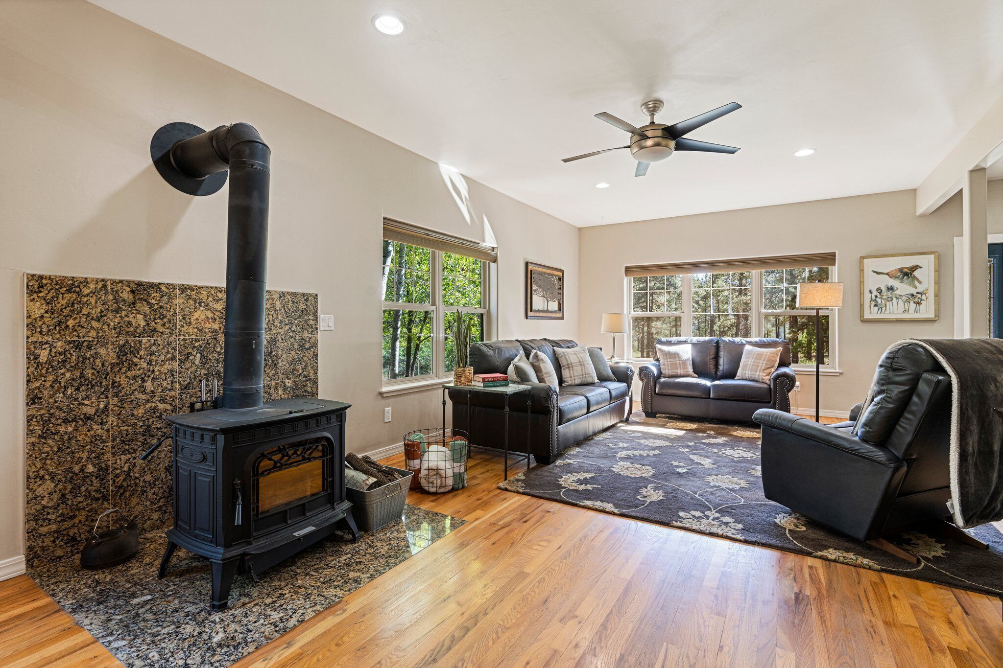 A living room with a wood-burning stove, leather sofa, and a ceiling fan.
