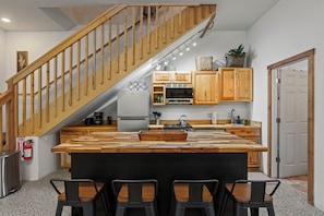 Eine Küche mit einer Holztreppe, einer zentralen Kochinsel mit Hockern, Holzschränken und einem Edelstahl-Kühlschrank.
