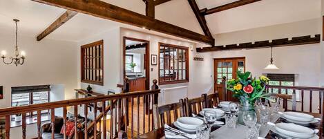 A dining area with a wooden table set for six, a chandelier, and a view of the kitchen through a glass door.
