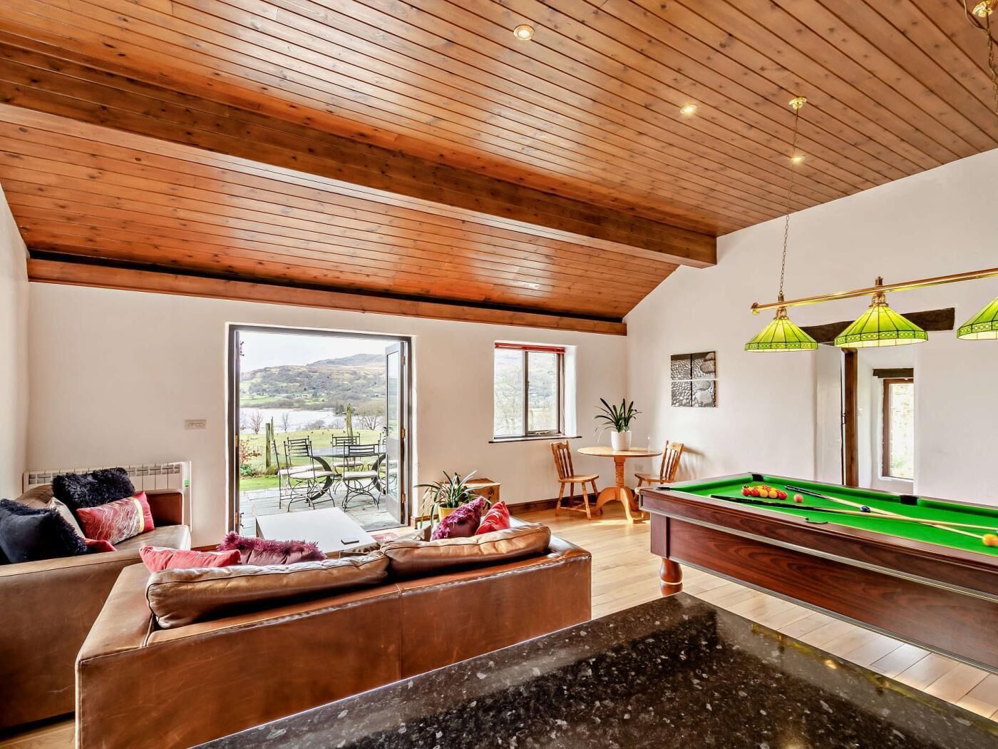 A room with a pool table, seating area, and a view of the outdoors.