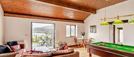 A room with a pool table, seating area, and a view of the outdoors.