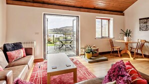 Amplia sala de estar con techo de madera, un sofá, una mesa de centro y vista a un jardín a través de un ventanal.