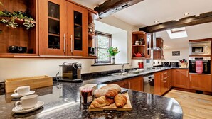 Una cocina con armarios de madera, encimera de granito, cafetera y una mesa con croissants y mermelada.