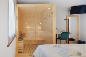 Ein Zimmer mit einem Holzschrank, einem Bett, einem Schreibtisch mit Stuhl sowie einem an der Wand befestigten Fernseher.