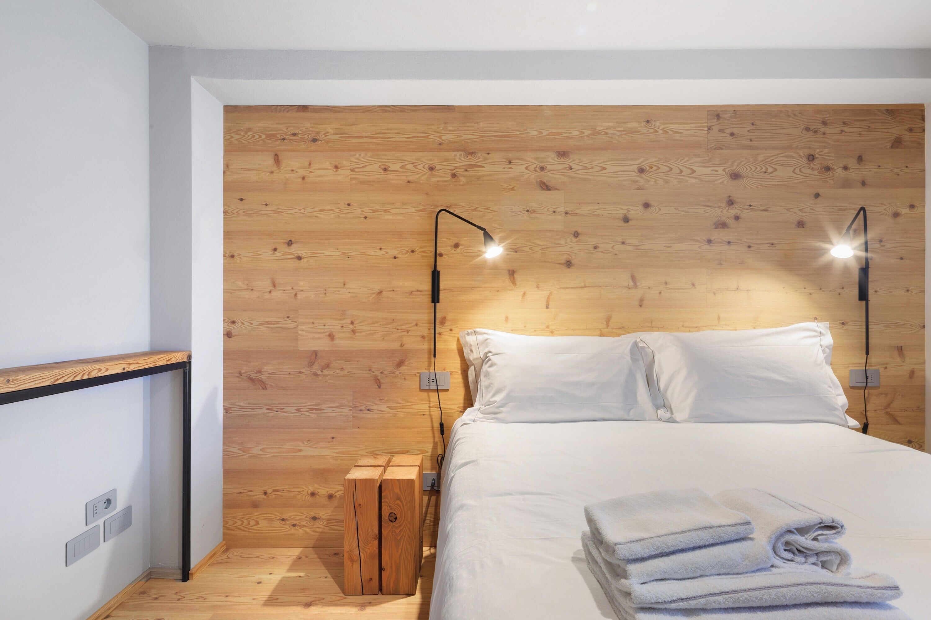 Ein modernes Schlafzimmer mit einem hölzernen Kopfende, einem Bett mit weißen Bettwäsche, zwei Nachttischlampen und einem Nachttisch aus Holz.