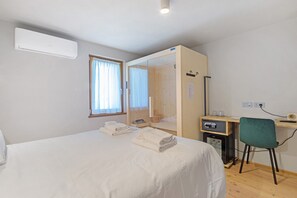 Une chambre d’hôtel comprenant un lit, un bureau, une chaise, une armoire et une fenêtre avec des rideaux.
