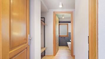 Ein enger Flur mit Holzboden, eine Holztür links und im Hintergrund ein Badezimmer mit Toilette und Spiegel.