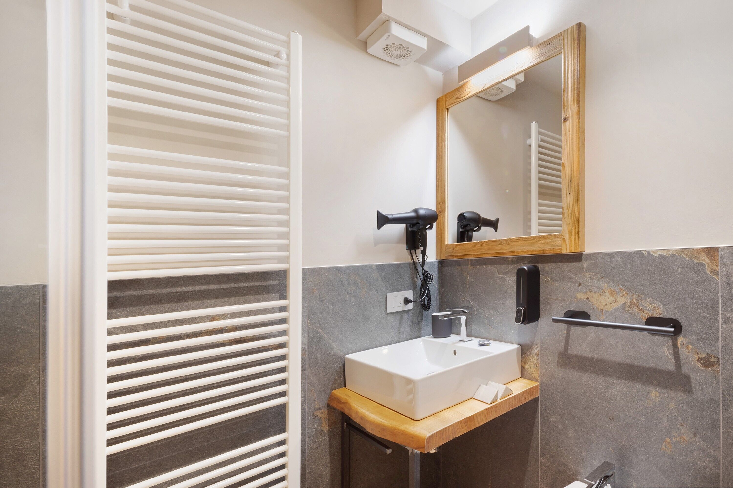 Un baño moderno con un lavamanos blanco, un espejo y un perchero para toallas.