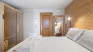 A hotel room with a wooden panel wall, a bed with white linens, a wooden wardrobe, and a glass shower enclosure.