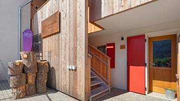 A wooden building entrance with a staircase, a red door, and a signboard.