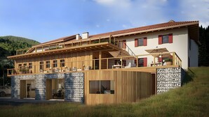 A modern two-story house with a wooden deck, stone facade, and a red-tiled roof.