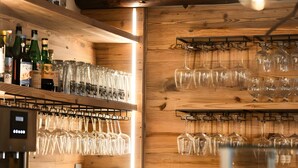 A bar area with shelves of liquor bottles and glasses, a coffee machine, and a wooden wall.