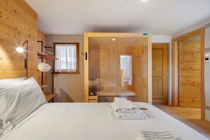 Ein Hotelzimmer mit hölzernem Kopfteil, einem Bett mit weißen Leinen, einem Nachttisch mit Lampe und einer Holztür zu einem Badezimmer.