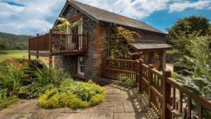 A stone house with a balcony, surrounded by lush greenery and a clear sky. - 1 Bed in Coniston (oc-lcc37) (Blawith)