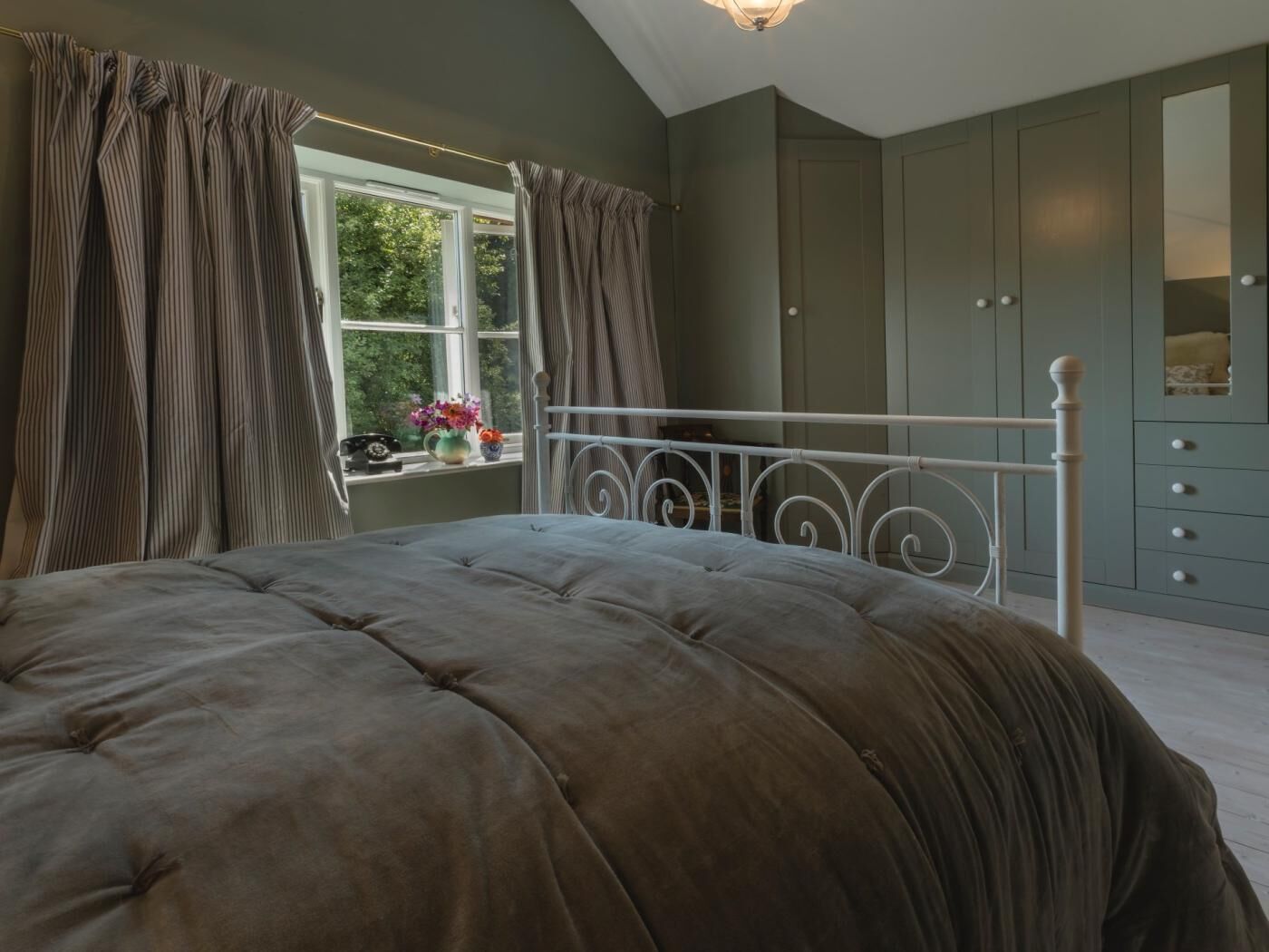 Ein Schlafzimmer mit einem Bett, einem Fenster mit Vorhängen, einem Schminktisch und einem Spiegel.