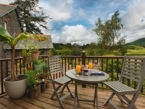 A wooden deck with a table and chairs, potted plants, and a scenic view of hills and trees. - 1 Bed in Coniston (oc-lcc37) (Blawith)