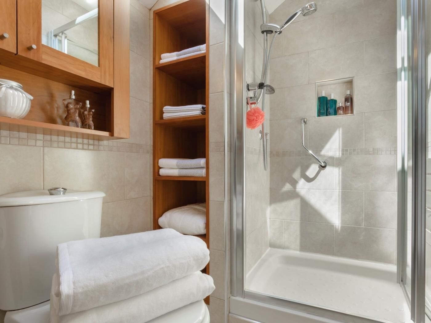 Een moderne badkamer met een douchecabine van glas, een toilet en een houten wastafelmeubel met planken.