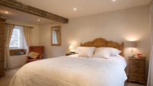 Um quarto com uma cama grande, duas mesas de cabeceira, uma cadeira, uma janela com cortinas e um espelho na parede.