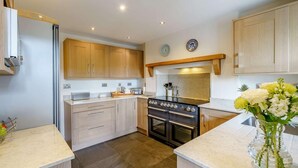 A modern kitchen with wooden cabinets, a built-in oven, and a countertop with a vase of flowers. - 4 Bed in Nr Hawkshead (oc-lcc33) (Near Sawrey)