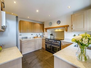 A modern kitchen with wooden cabinets, a built-in oven, and a countertop with a vase of flowers. - 4 Bed in Nr Hawkshead (oc-lcc33) (Near Sawrey)