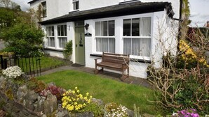 A white building with a green door, a bench outside, and a garden with various flowers. - 4 Bed in Nr Hawkshead (oc-lcc33) (Near Sawrey)
