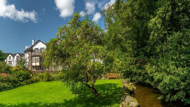 Une maison traditionnelle en pierre, dotée d’une pelouse bien entretenue et traversée par un petit ruisseau.