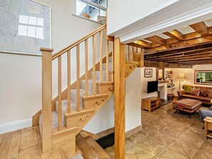 Eine Holztreppe führt zu einem Erkerbereich mit Kamin, einer Ledersofa und einer Karte an der Wand.