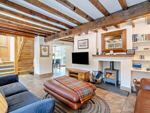Ein gemütliches Wohnzimmer mit Kamin, Holzbalken, Fernseher und Bücherregal.