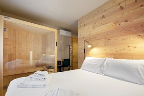 Hotellihuone, jossa on puinen seinä, valkoisilla lakanoilla varustettu sänky, työpöytä tuolilla ja näkyvissä oleva ilmastointilaite.