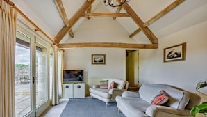Un salon avec un plafond en bois, un canapé, un téléviseur et une vue dégagée sur l’extérieur grâce à une grande fenêtre.