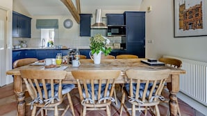 Une cuisine avec des meubles de couleur bleu foncé, une table à manger en bois avec des chaises, une horloge au mur et un radiateur.