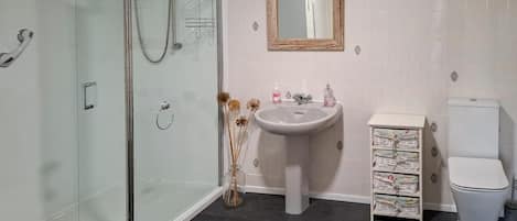 A bathroom with a glass-enclosed shower, a pedestal sink, a toilet, and a storage unit with drawers.