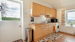 A compact kitchen with wooden cabinets, a washing machine, and a window with a view. - 2 Bed in Dundee (oc-58026) (Wellbank)