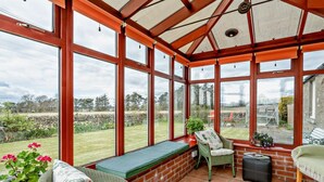 A conservatory with large windows, a green cushioned bench, wicker furniture, and a brick wall. - 2 Bed in Dundee (oc-58026) (Wellbank)