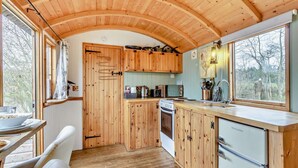 Een houten interieur met een keuken, een eethoek en een raam met uitzicht op bomen.