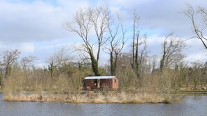 Een klein, afgelegen huisje aan het water, omgeven door bomen en begroeiing.