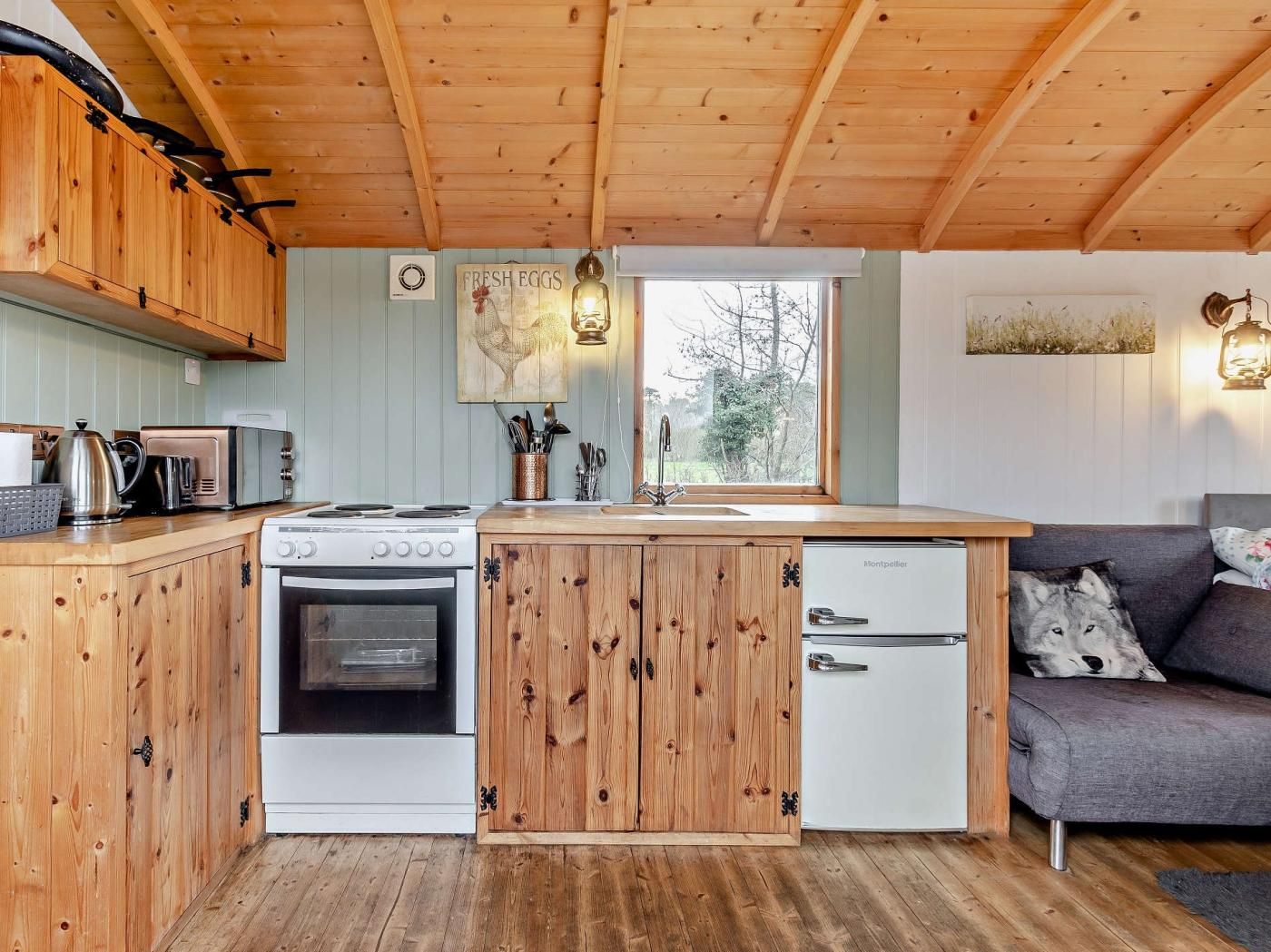 Une cuisine compacte dotée de meubles en bois, d’une cuisinière, d’un évier et d’un réfrigérateur. Une fenêtre laisse entrer la lumière naturelle et offre une vue sur l’extérieur.