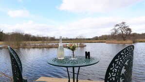 Een tafel bij een meer, met stoelen, een fles en een vaas met bloemen.