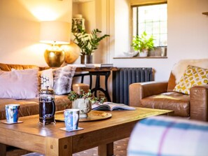 Ein gemütliches Wohnzimmer mit Couch, Holztisch, Lampe und einem Fenster mit Pflanzen.