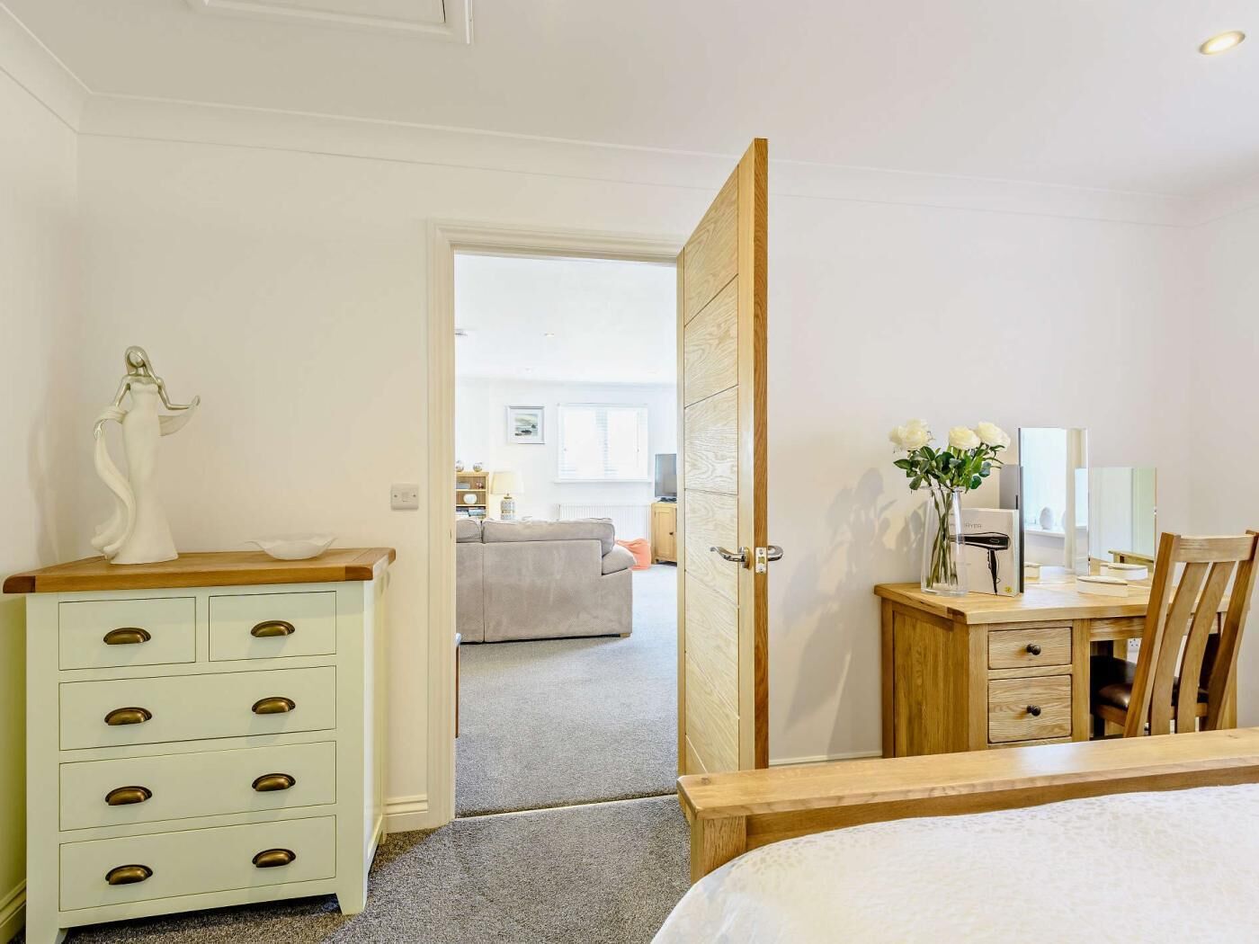 A bedroom with a bed, a dresser, a desk, and a door leading to another room.