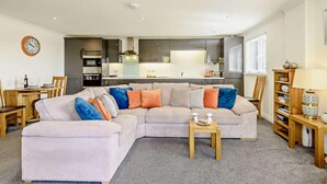 Ein modernes Wohnzimmer mit einer Eckcouch, einem Esstisch und einer Küche im Hintergrund.