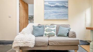 A beige sofa with patterned cushions, a knitted throw, and a framed ocean view painting.