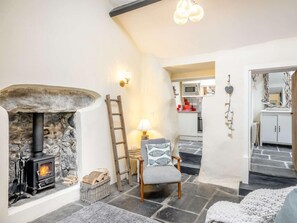 A cozy living room with a stone fireplace, a wooden ladder, a comfortable chair, and a kitchen visible through an open doorway. - 2 Bed in Llwyngwril (oc-58564) (Llwyngwril)