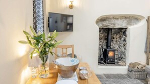 A dining area with a table set for two, a fireplace, a television, and a plant. - 2 Bed in Llwyngwril (oc-58564) (Llwyngwril)
